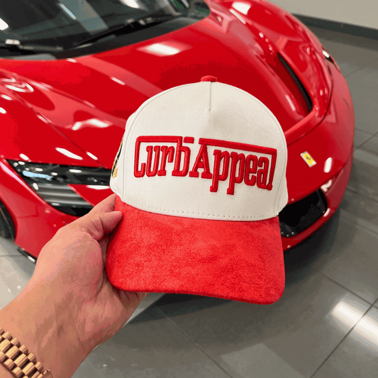 The Winner's Circle Hat with red suede bill, embroidery, and 3D stitching in front of red sports car.