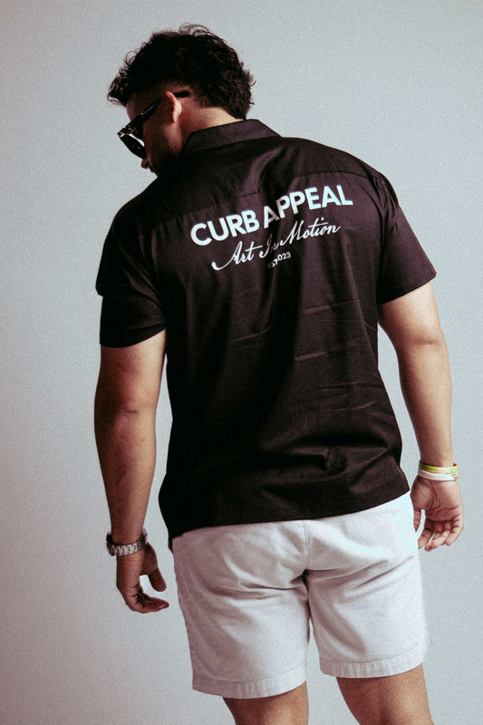 Art In Motion shirt with back logo design, modeled by a person in sunglasses and shorts.