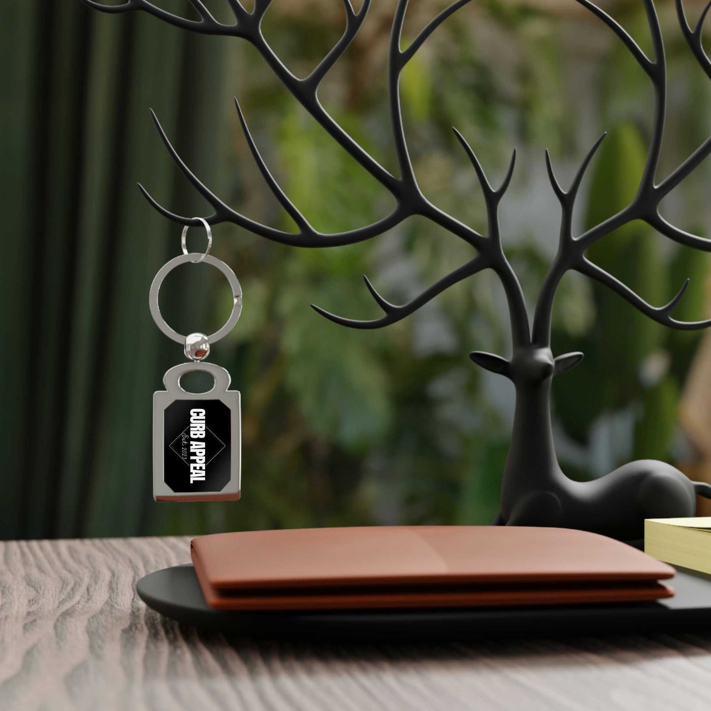 Metallic logo keychain with car emblem hanging on decorative black deer antler stand on wooden table with brown wallet and green blurred background