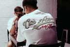 White Donk Tee with "Curb Appeal Art in Motion" design worn by a seated person.