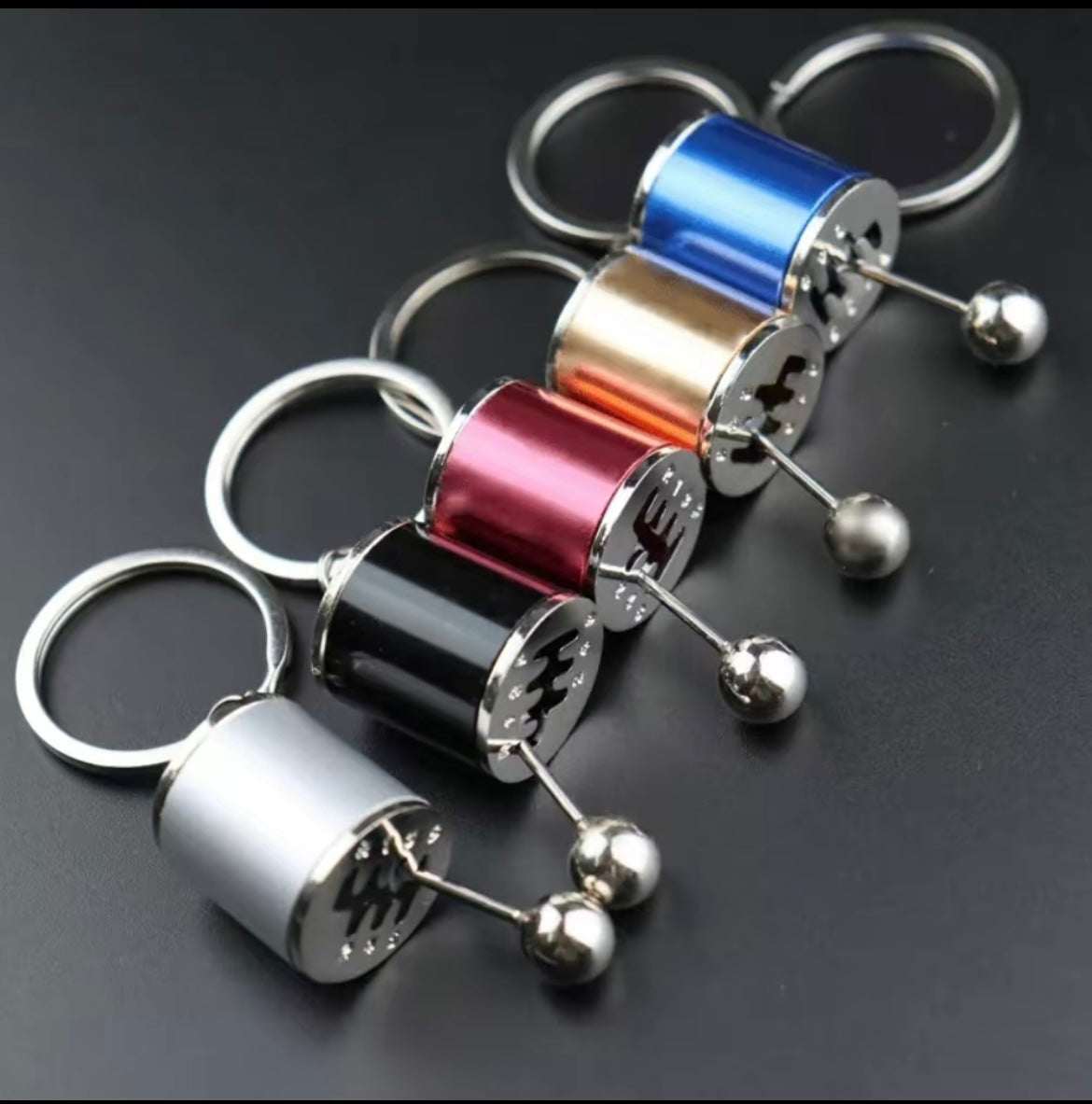 Shifter keychain in various metallic colors mimicking a sports car gear shifter, designed for car enthusiasts.