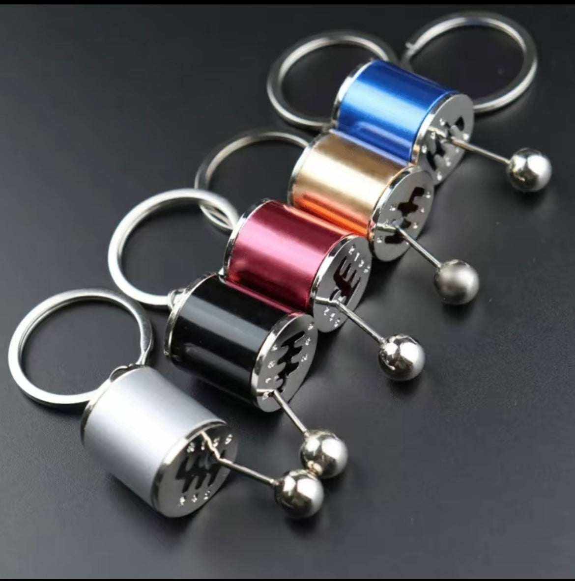 Shifter keychain in various metallic colors mimicking a sports car gear shifter, designed for car enthusiasts.