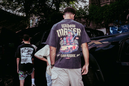 Widow Maker Tee with bold automotive graphics, worn by a model outdoors near vehicles.