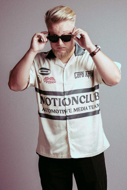 Motion Club Polo shirt in cream with automotive team design, modeled by a man wearing sunglasses.