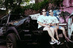 Unisex models wearing Donk Tee with full-color graphic, sitting on a truck, showcasing urban style.