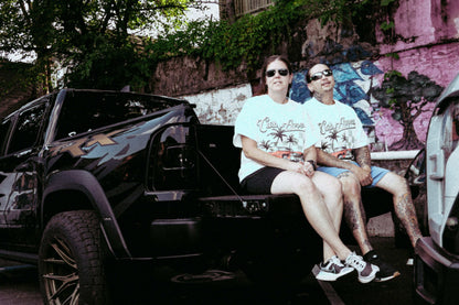 Unisex models wearing Donk Tee with full-color graphic, sitting on a truck, showcasing urban style.