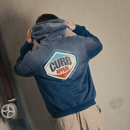 Loose fit Pit Stop Hoodie in blue with Curb Appeal patch, modeled in urban setting.