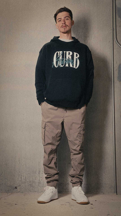 Unisex soft high neck hoodie in black, featuring front design, worn by a model with beige cargo pants.