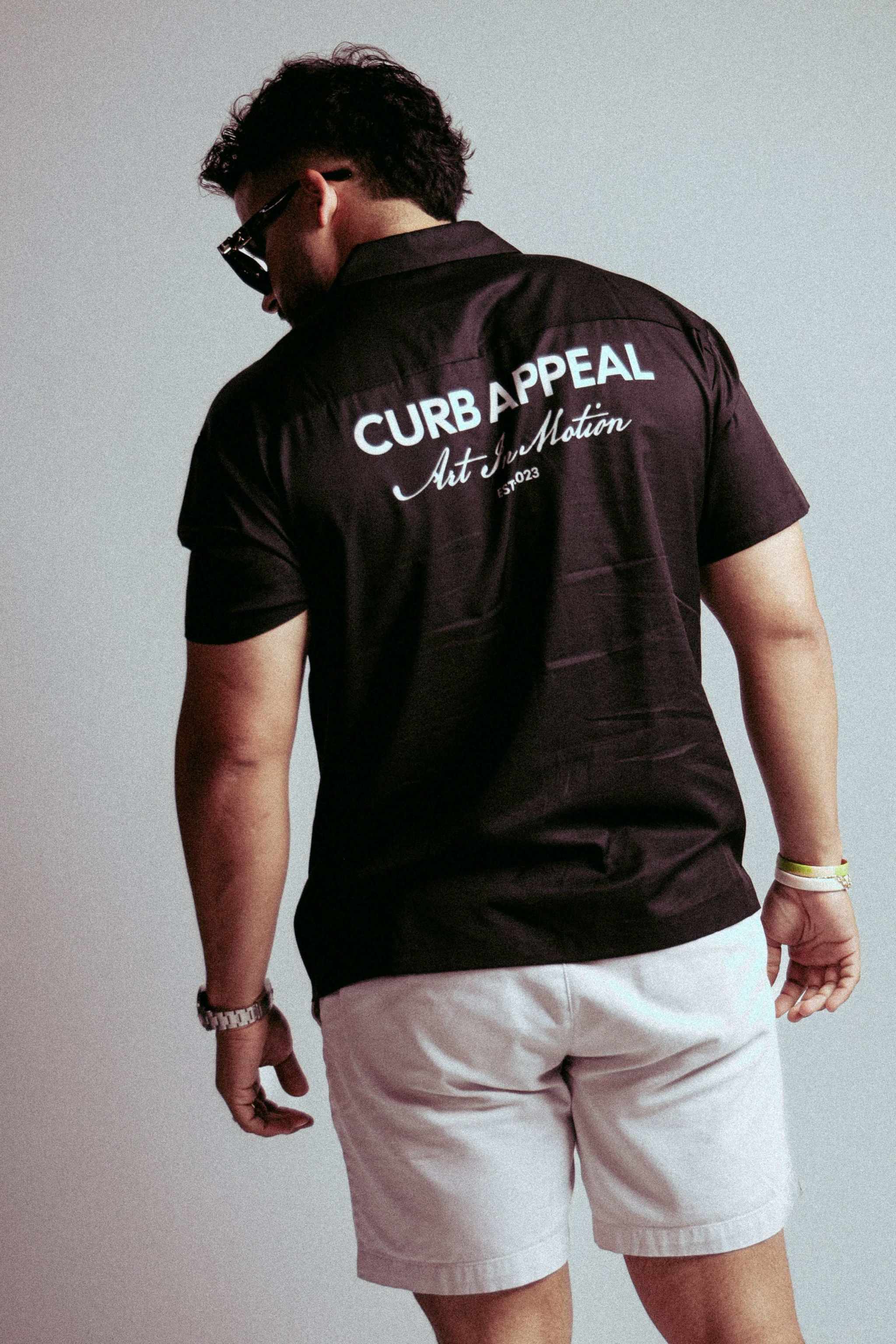 Art In Motion shirt with back logo design, modeled by a person in sunglasses and shorts.