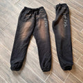 Black Art In Motion Pants on wooden floor, featuring automotive-inspired design with elastic waistband and cuffs.