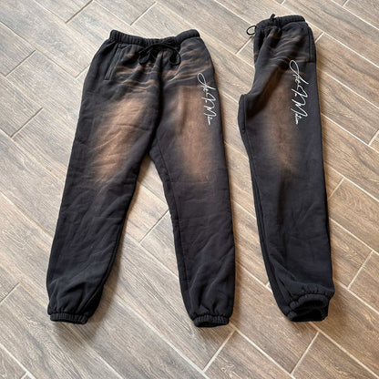 Black Art In Motion Pants on wooden floor, featuring automotive-inspired design with elastic waistband and cuffs.