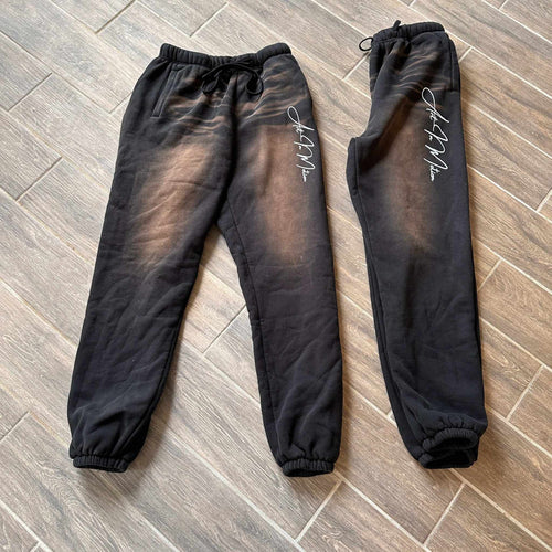Black Art In Motion Pants on wooden floor, featuring automotive-inspired design with elastic waistband and cuffs.