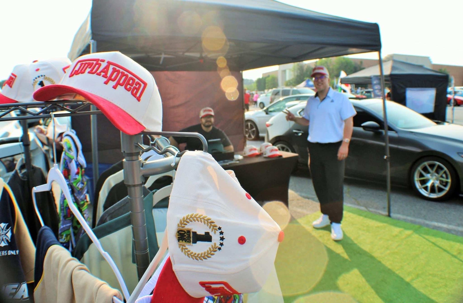 The Winner's Circle Hat with red suede bill and 3D stitching displayed at a car show booth.